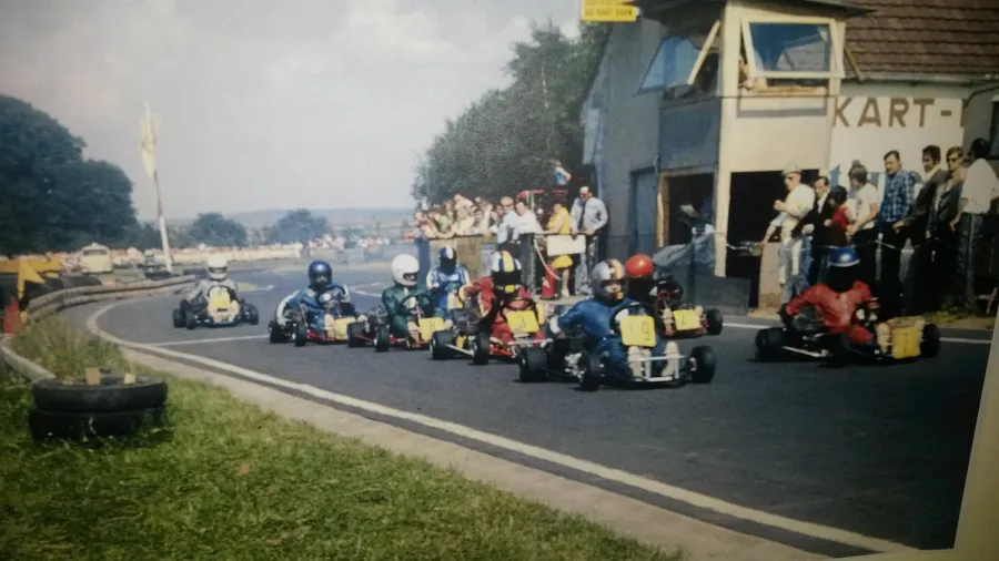 Historische Aufnahme: Karts beim Start vor dem Kartbahn-Gebäude, Zuschauer am Rand.