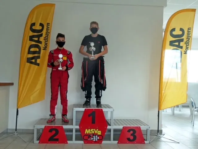 Drei junge Fahrer mit Pokalen auf dem Siegerpodest.