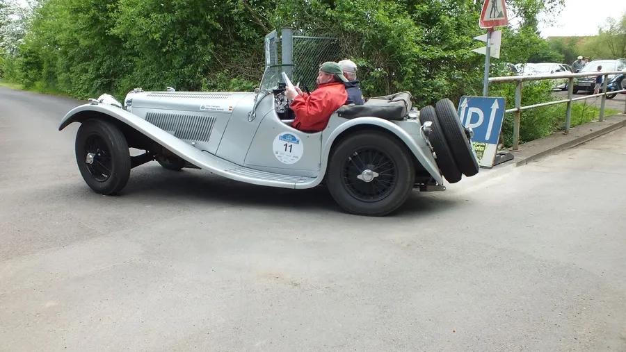 Silberner Oldtimer-Roadster mit zwei Insassen.