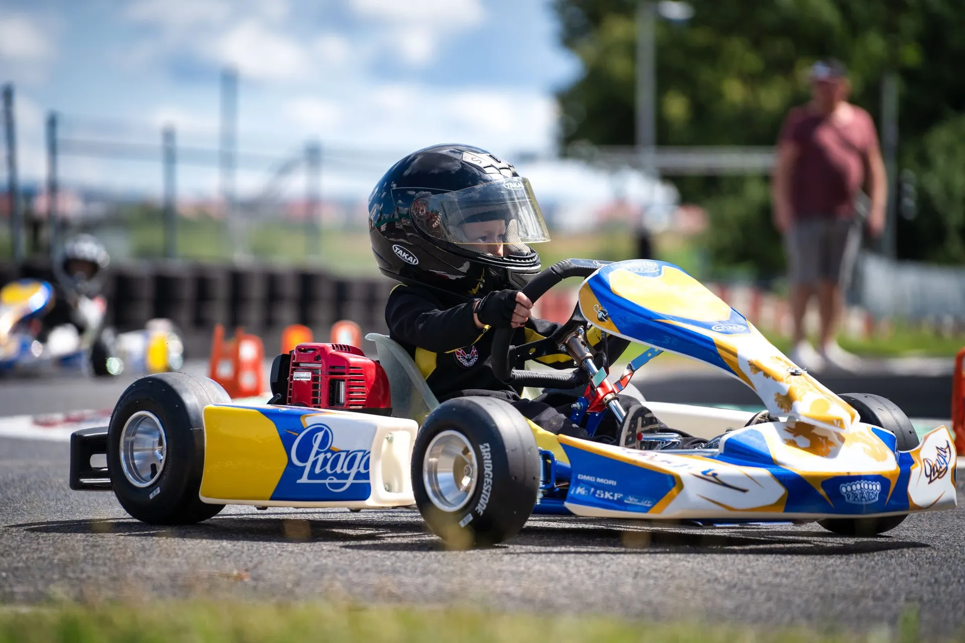 Kind mit Helm sitzt am Steuer eines blau-gelben Puffo-Karts auf der Strecke.