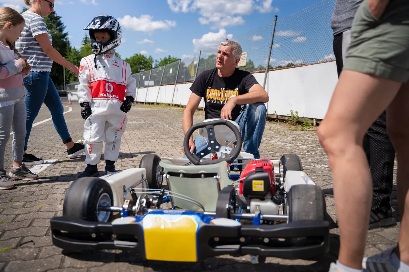 Ein Trainer erklärt einem Kind im Rennanzug das Puffo-Kart, daneben schauen Eltern und Geschwister zu.