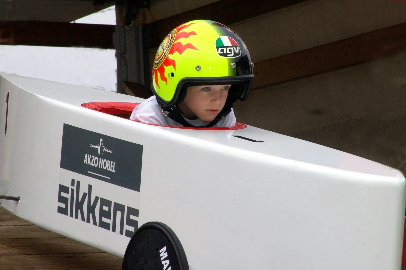 Junge mit buntem Helm sitzt konzentriert in seiner weißen Seifenkiste.