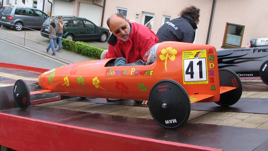Ein Helfer schiebt eine orangefarbene Seifenkiste mit der Startnummer 41 auf die Rampe.