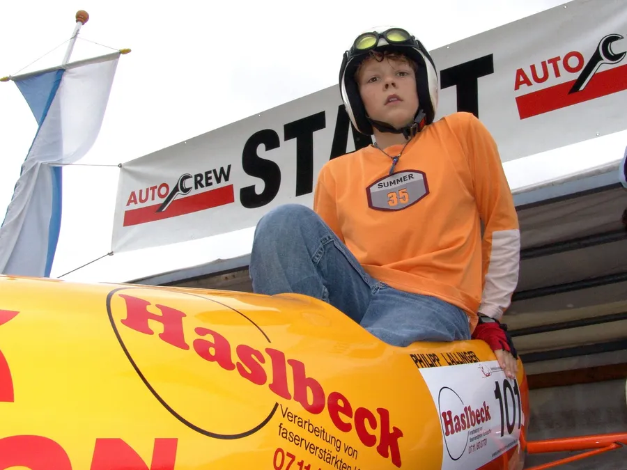 Junge mit Helm sitzt lachend auf seiner Seifenkiste unter dem Start-Banner.